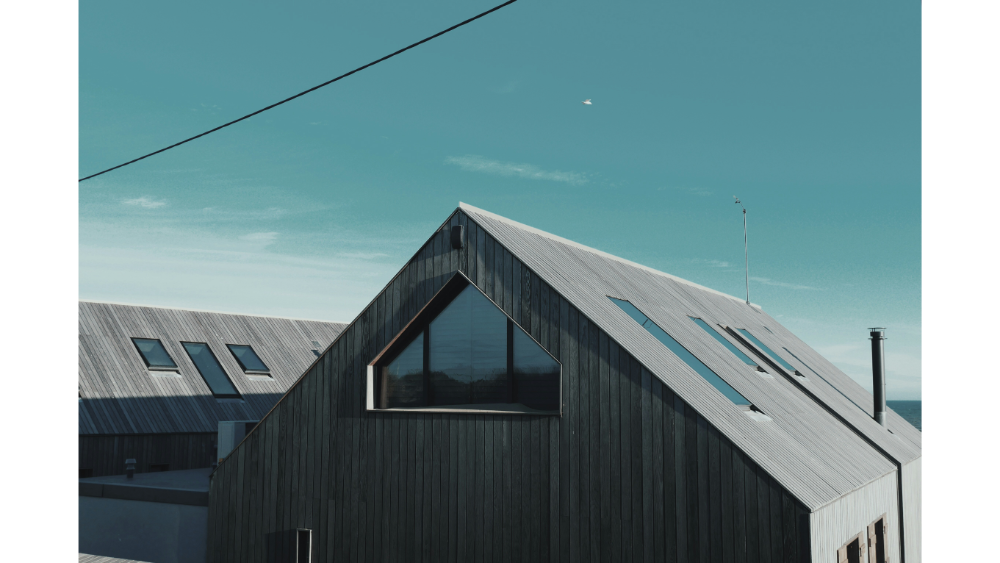 Modern home with a steep gable roof and vertical wood siding, featuring skylights and large windows under a teal sky.
