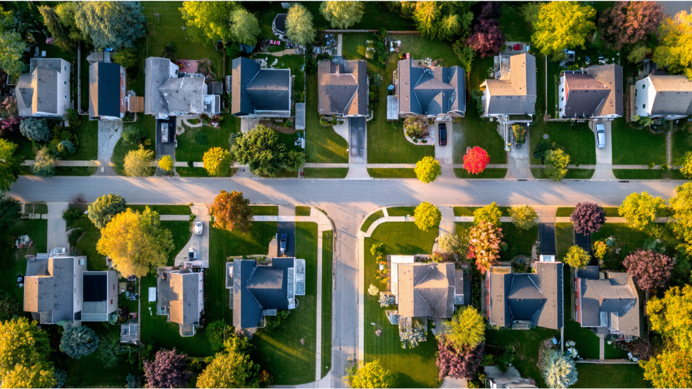 Aerial view of a quiet suburban neighborhood showing homes, streets, and rooftops with varied shingle colors