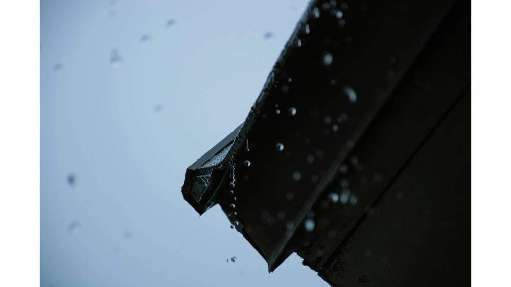 Close-up of rainwater dripping from the edge of a roof during a storm, with droplets captured mid-air.